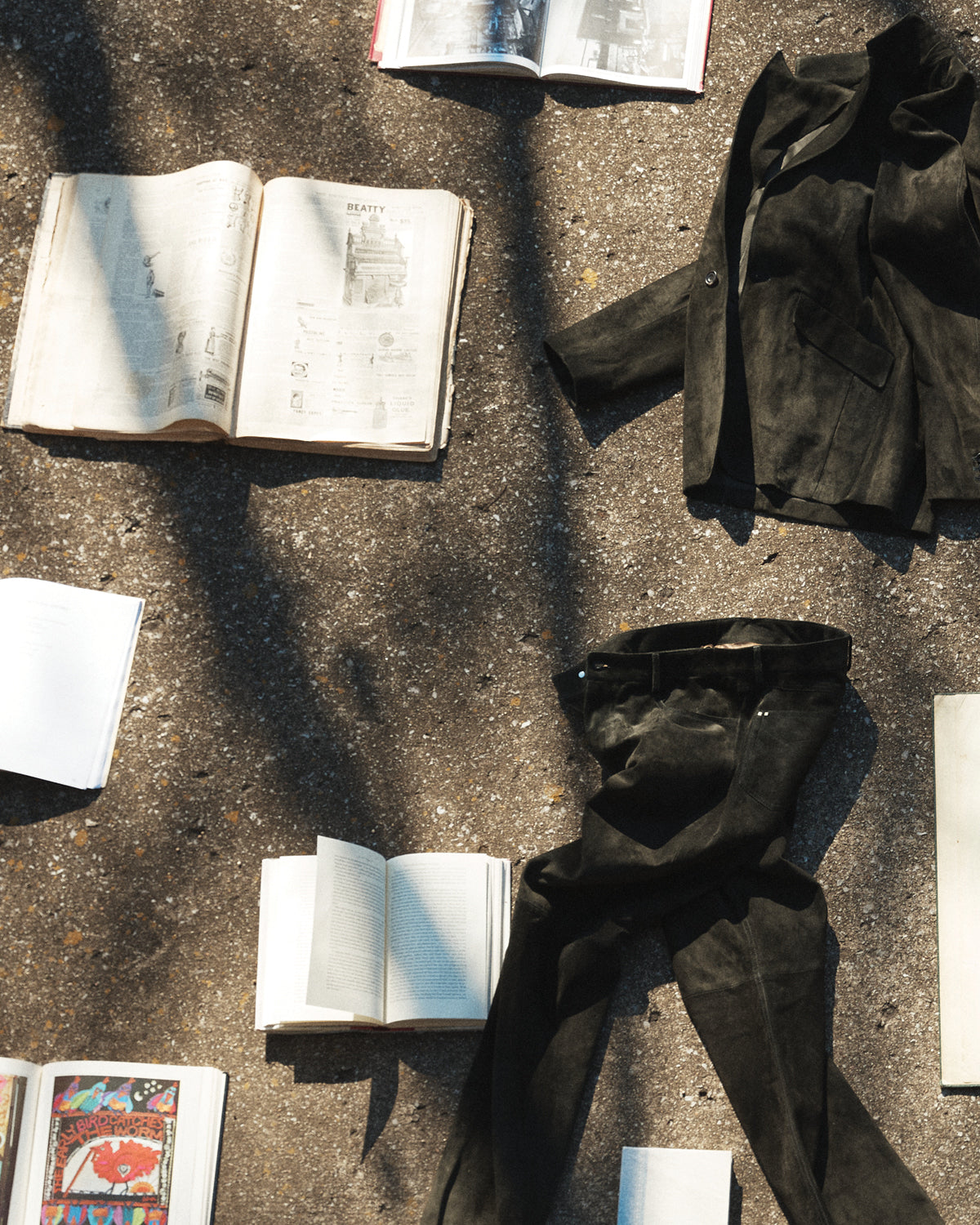 Savas suede pants and jacket lying on the concrete surrounded by books