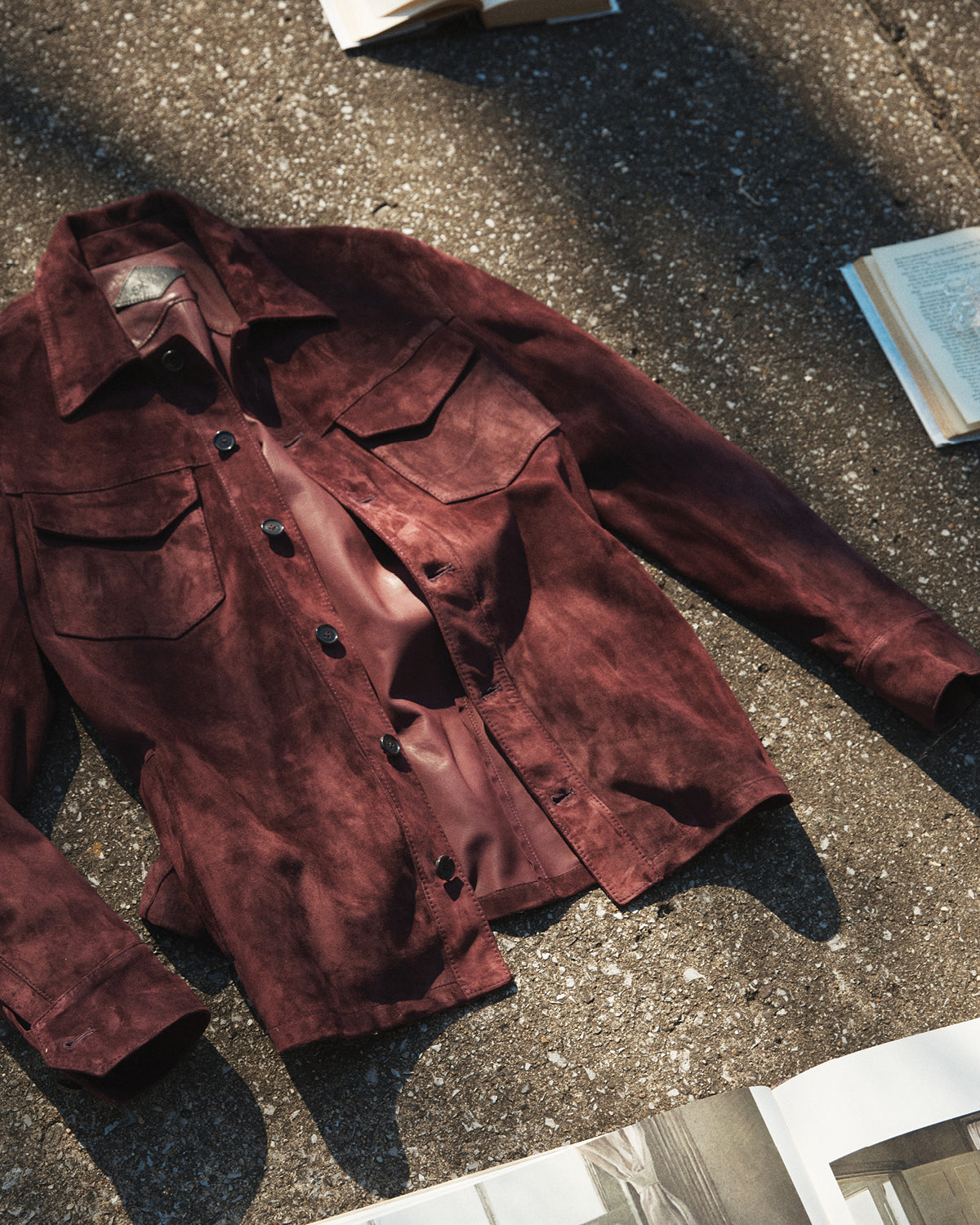 a maroon suede Savas jacket lying on the concrete surrounded by books