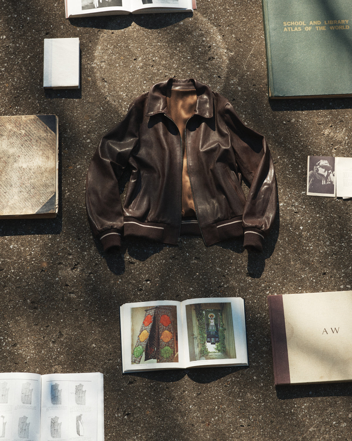 A brown Savas bomber jacket lying on the concrete with books around it